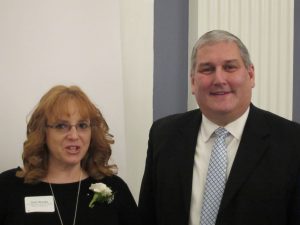 Woman in black dress wearing a white corsage standing next to a man in a dark suit.