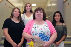 Three high school girls flank woman in school hallway.