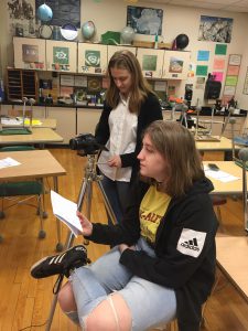 a high school student uses a video camera while another conducts an interview in a high school science classroom