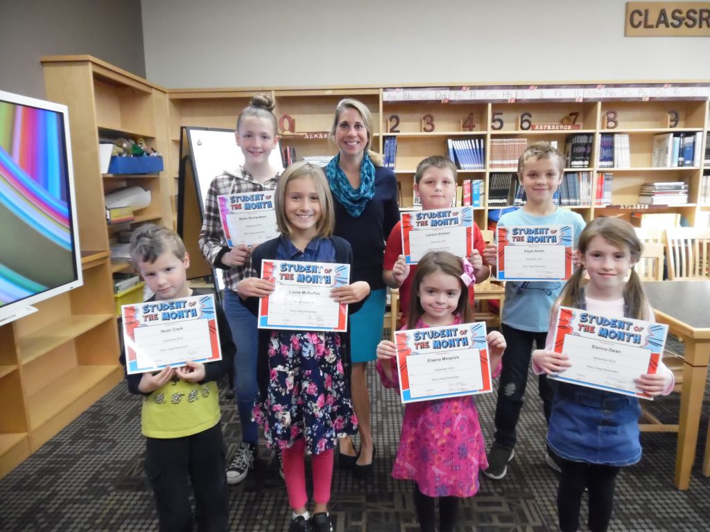 Seven students and an elementary school principal stand in two rows in a school library