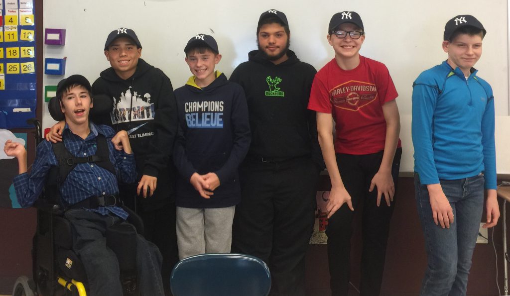 six students in yankees hats stand before a whiteboard in a classroom