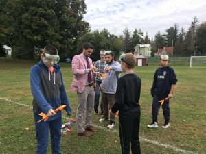 five students and a teacher hold rockets outside while wearing safety goggles