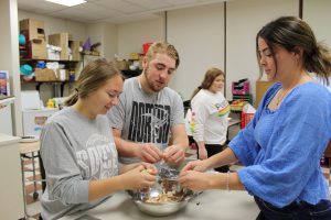 three high school students shred chicken into a bowl in a high school food science classroom
