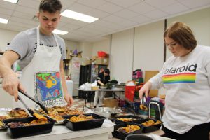 two high school students spoon barbecue chicken into take-out containers in a high school food science classroom