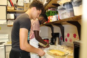 two high school students cut up cornbread in a high school food science kitchen