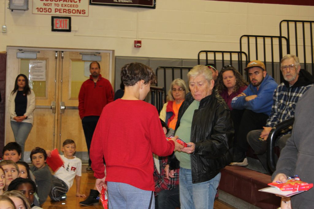 elementary student hands a veteran a small gift in a school gymnasium