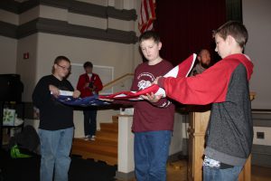 three seventh graders show the proper way to fold an American flag in a school auditorium