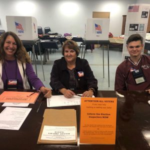 two adults and a high school student sit at a table at a poll site in a senior center