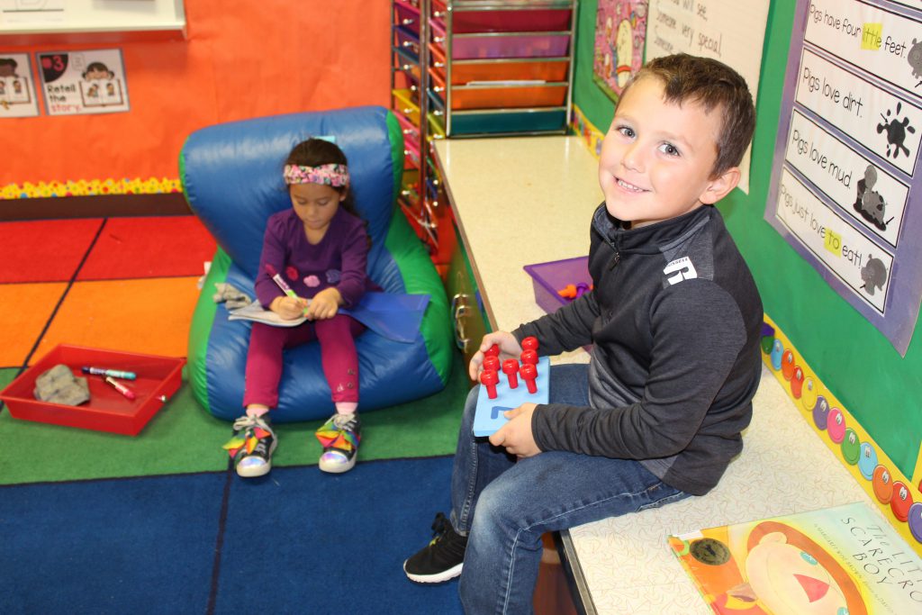 kindergarten student sits on a bean bag while a classmate is seated on a counter