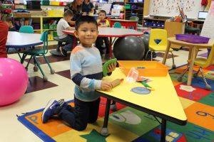 kindergarten student kneels at a table while playing with Play-Doh