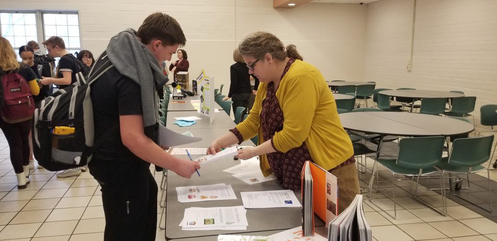 teacher talks to a high school student at a table in a cafeteria