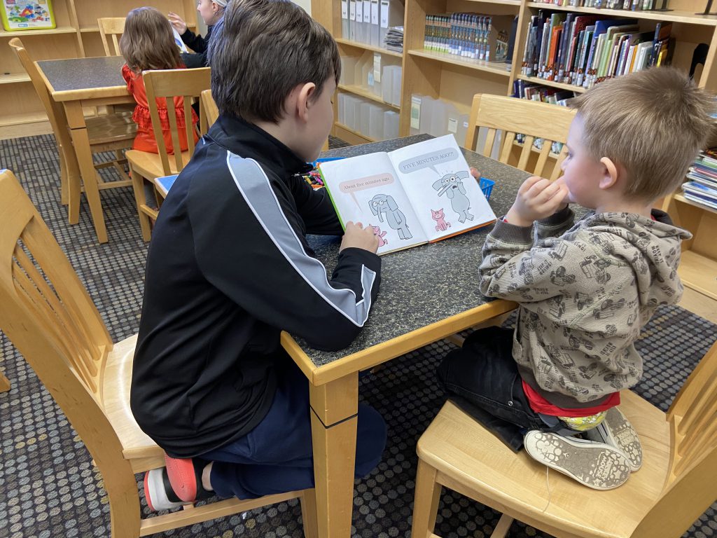 fifth grade student reads to a pre-k student in a school library