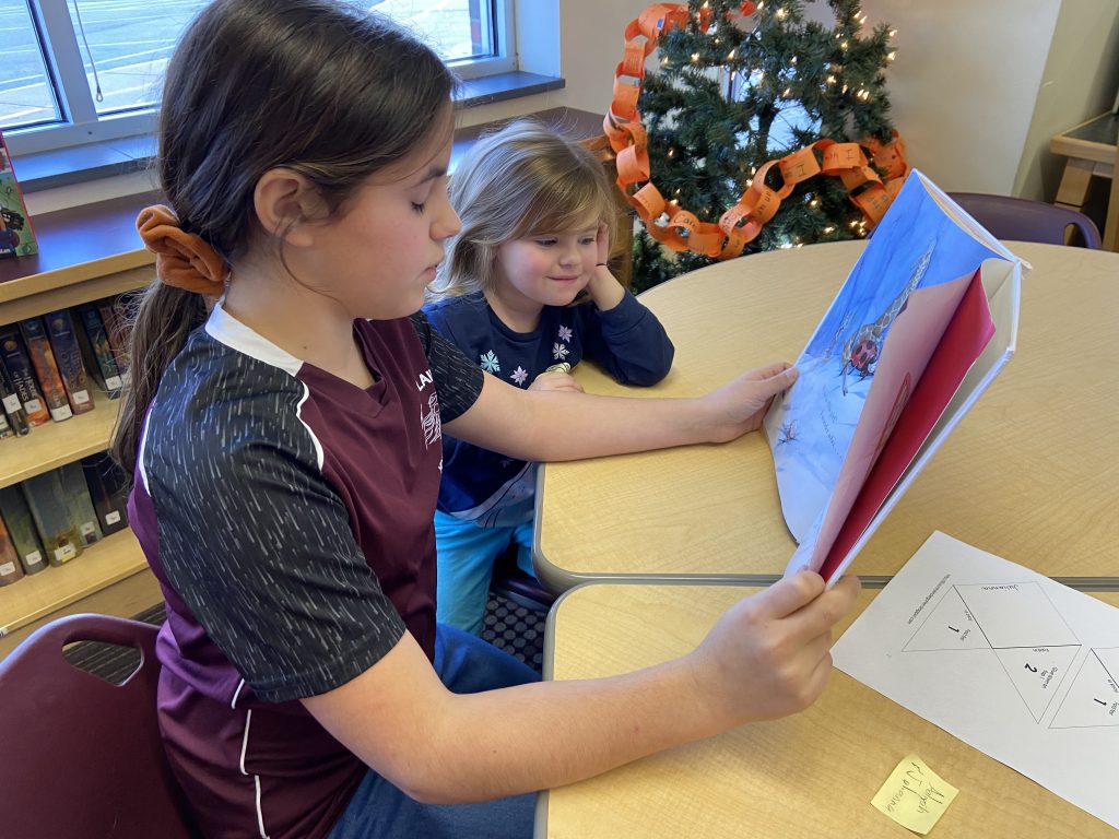 fifth grade student reads to a pre-k student in a school library