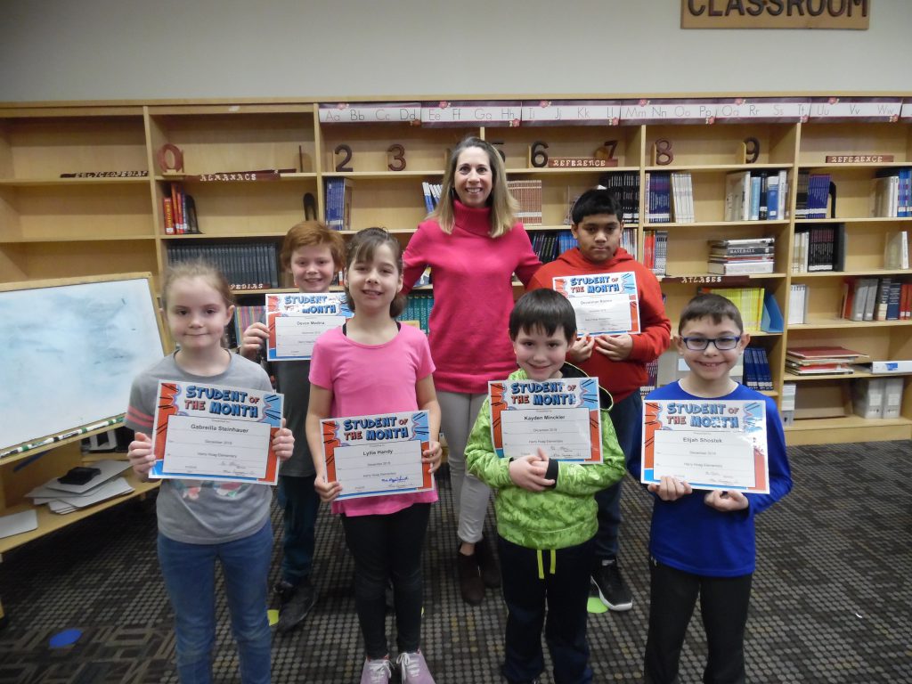 group of students stand with an elementary principal in a school library