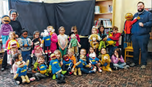 group of elementary students pose in a school library holding puppets