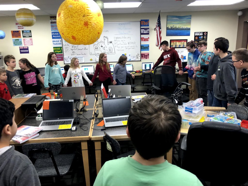 Students hold hands in a circle in a computer lab
