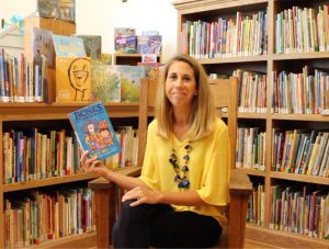 school principal holds picture book seated in a chair in a school library