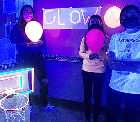 students holding balloons in blacklighted classroom