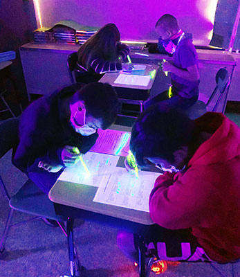 students working at desks in blacklighted classroom