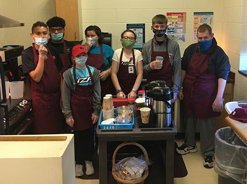 students standing in their classroom's kitchen area behind the coffee cart