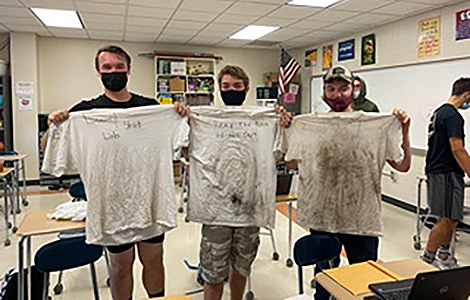 3 students holding up their well-worn t-shirts