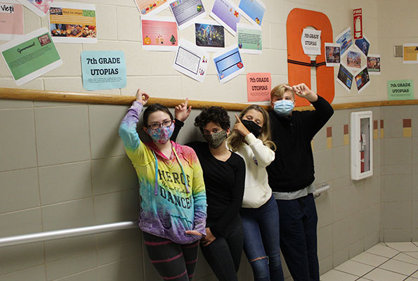 4 students point to their Utopia Projects posted on the wall above them