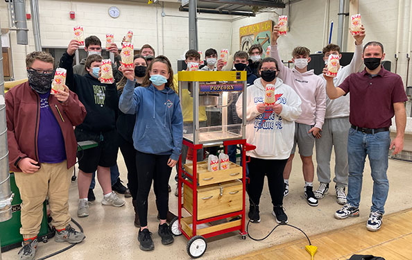 students and teachers holding popcorn bags around cart