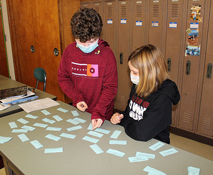 2 students standing at table matching slips of paper