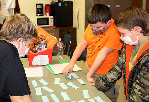 three students standing at table matching slips of paper