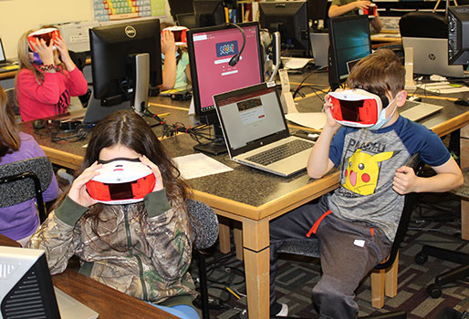 students seated at work tables looking into VR goggles