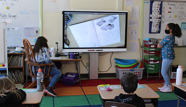 2 students at smart board with their book on it