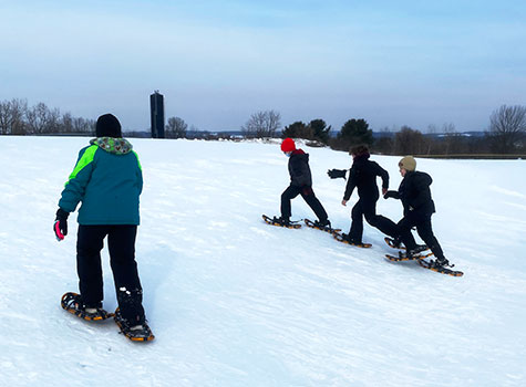 students and teacher snowshoeing on a hill