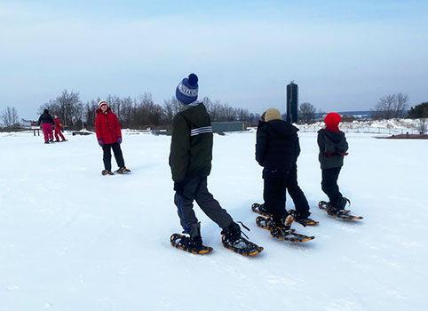 students and teacher snowshoeing on a hill