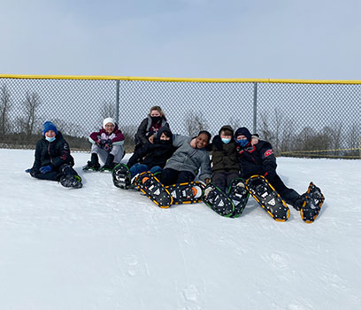 students in a group wearing snowshoes, sitting on snow 