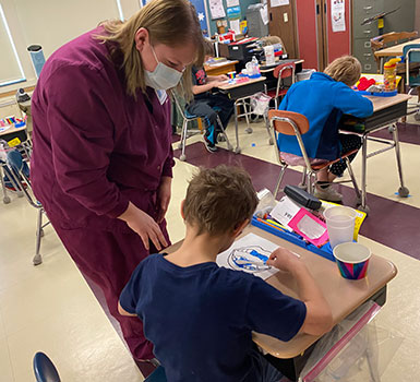 Danielle teaches a student about proper brushing as they paint teeth on paper