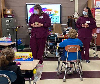 2 adults talk in front of classroom to students