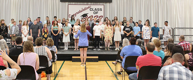 students singing on stage with teacher conducting