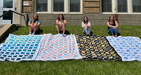 4 students sitting behind their quilts