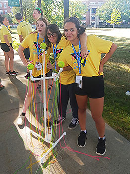 3 students standing by a frame with strings and a ball