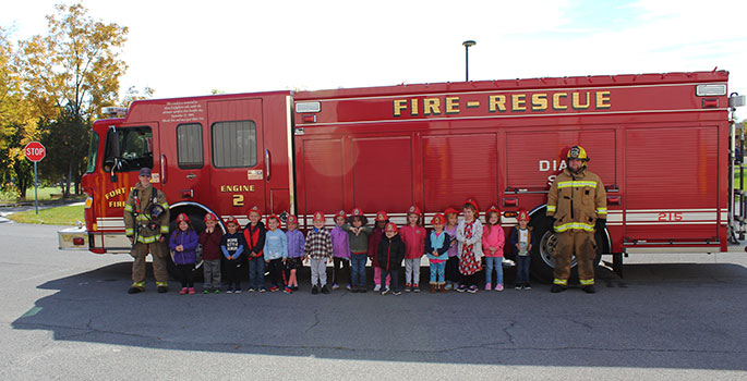 firefighters and children stand in front of fire truck
