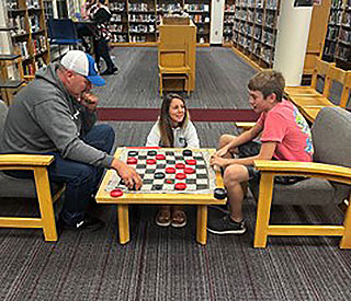 adults and student playing checkers in the library