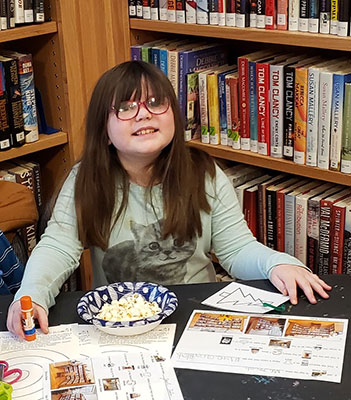 student seated at table smiling with artwork in front of them