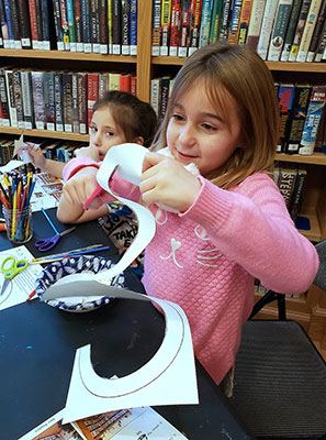 student cutting paper to create a snow person