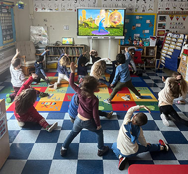 students practicing yoga poses on a rug in front of a video screen