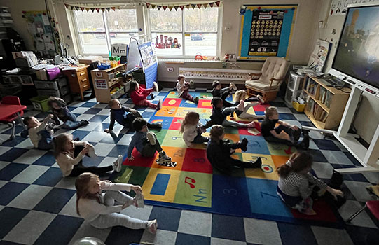 students practicing yoga poses on a rug in front of a video screen