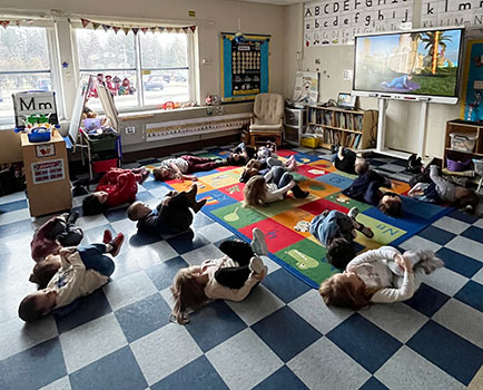 students practicing yoga poses on a rug in front of video screen