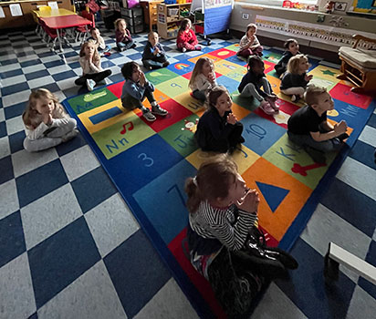 students practicing yoga poses on a rug in front of video screen