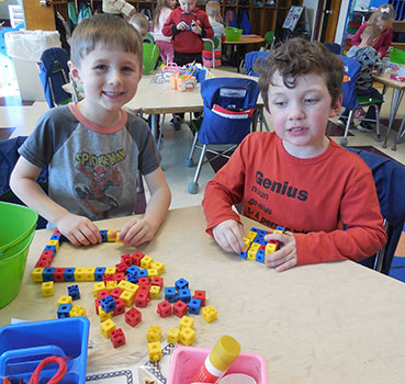 2 students seated at table, counting Legos