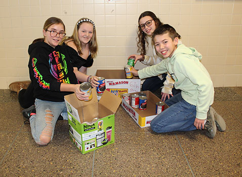4 students putting cans and package of food into a box