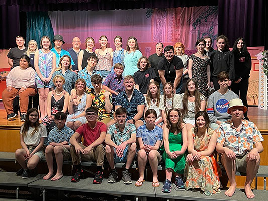 group of students in the cast and crew standing and sitting in front of stage